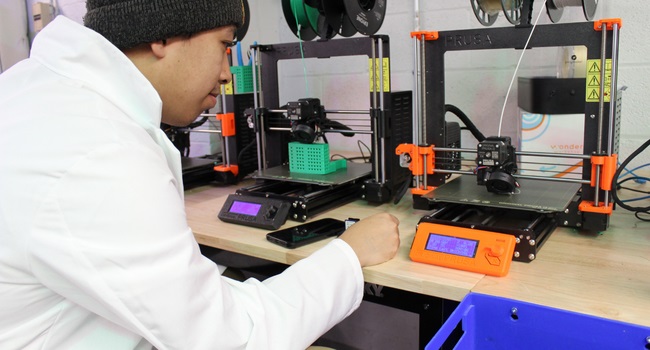 A man in a lab coat operating two 3D printing machines
