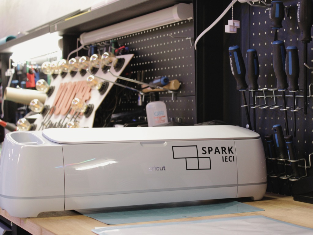 A Cricut machine with a Spark logo on the front sitting on a workbench