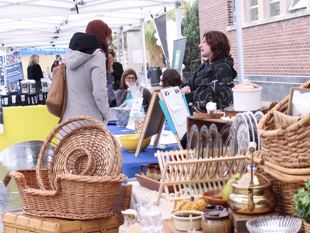 Two women speaking in an open market with an arrangement of wicker items in the foreground