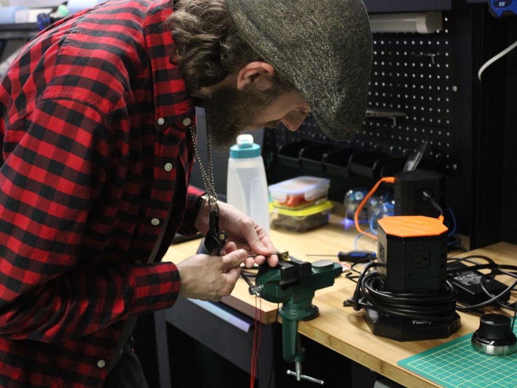 A man placing a small metal item in a bench vise